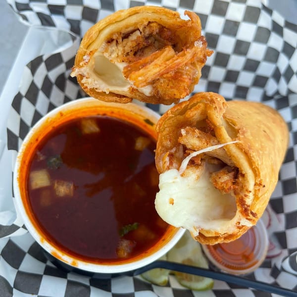 Two crispy El Burro Loco birria egg rolls with melted cheese, served with a side of consommé.